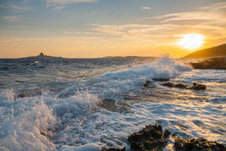 Waves splashing rocky beach at sunset on island Hvar, Croatia. Lighthouse Pokonji dol in the back.